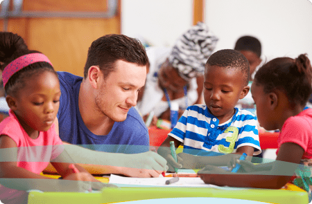 A teacher and three children sit at a classroom table together while they color.